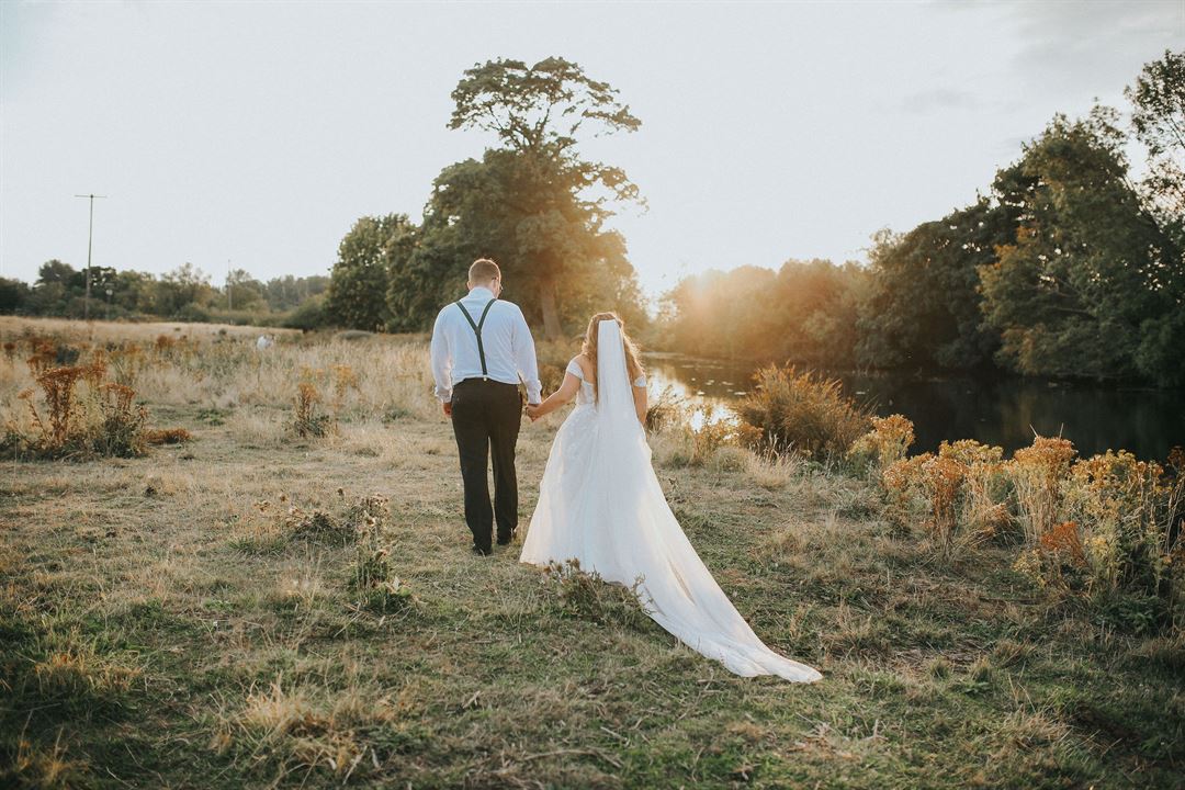 The couple walking through the field to the creek at golden hour